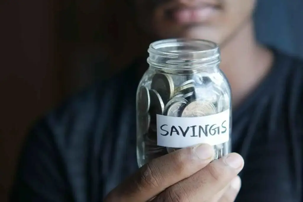 A person holding a jar of coins with the word savings written on it.