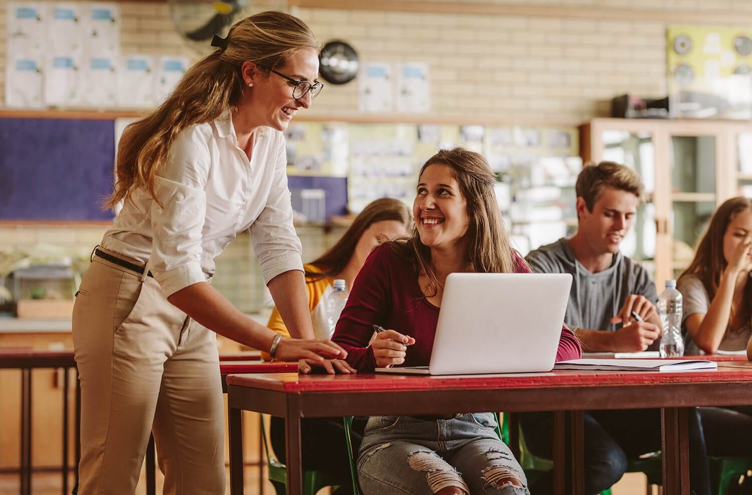 Two women are sitting at a table and one is using her laptop.