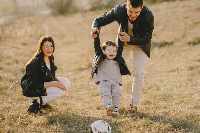 A man and woman watching a young boy play with a soccer ball.